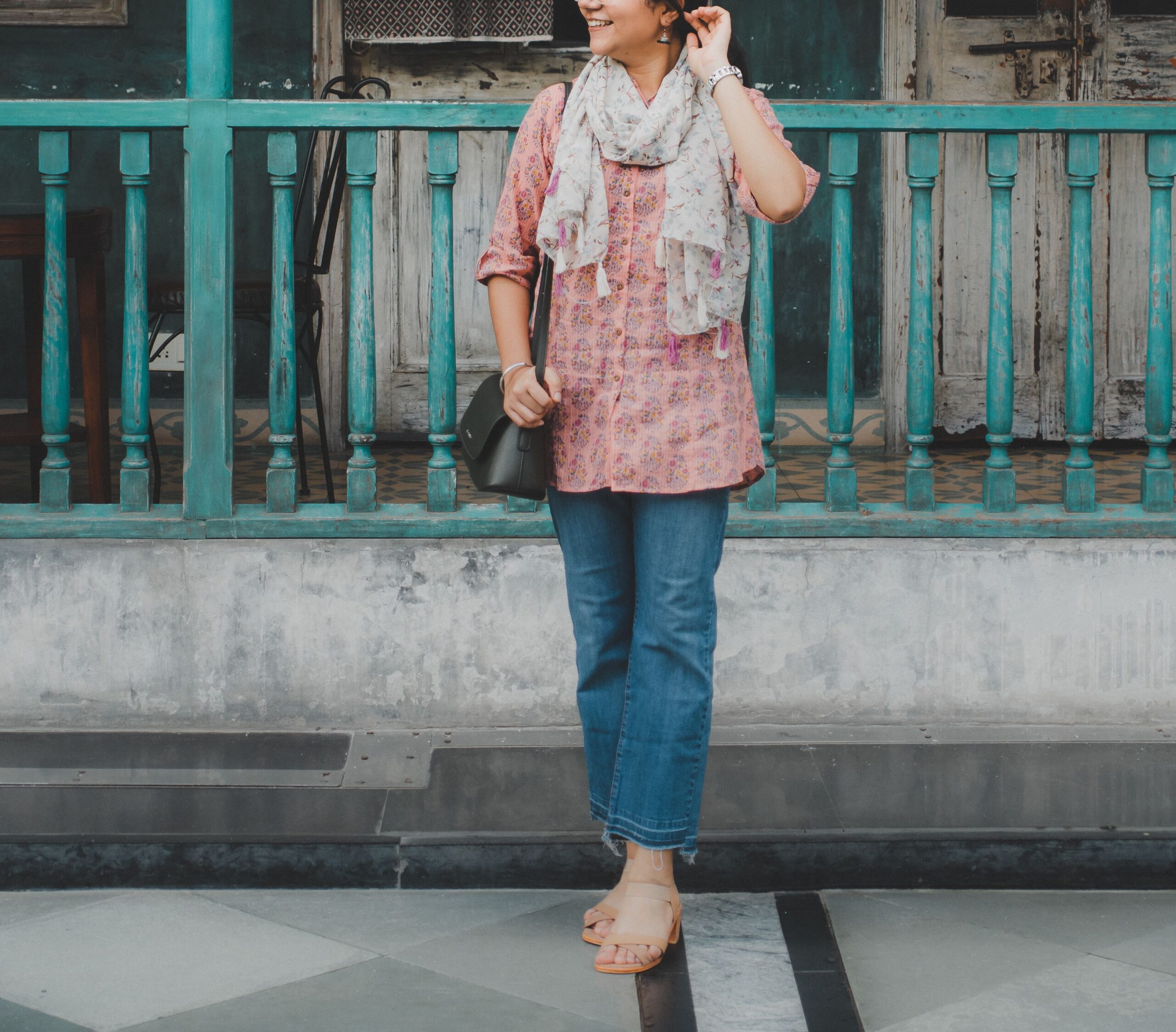 Woman in casual fashion with jeans and scarf posing against an urban backdrop.